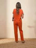 woman wearing orange 100 cotton total comfort two-piece set from the back standing on woven mat against beige background