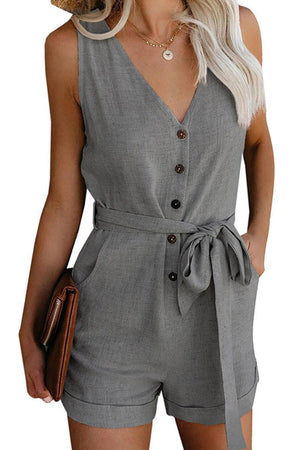 Woman wearing gray sleeveless V-neck layered romper with waist tie and pockets holding brown clutch