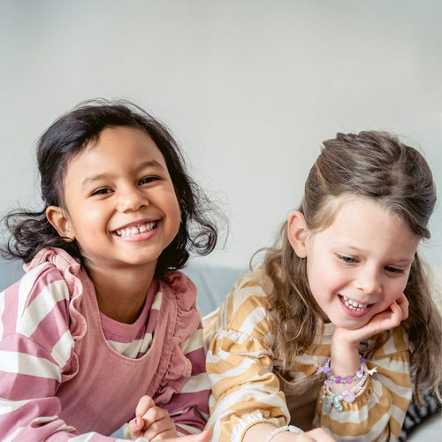 Two smiling children making bracelets with a kids bracelet-making kit, fostering creativity and motor skills.