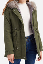 Women wearing olive green fur collar fleece coat with hood and adjustable drawstrings over white sweater and blue jeans