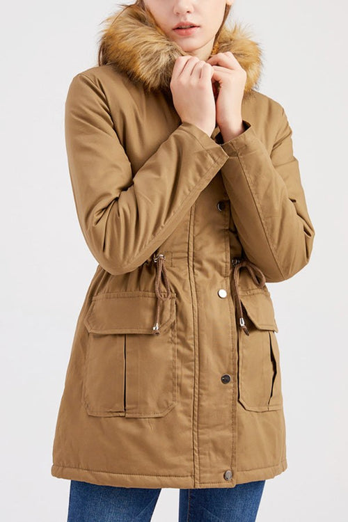 Woman wearing large hooded velvet coat with fur collar and front pockets in brown color