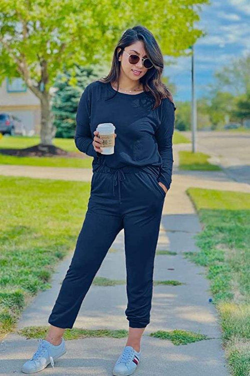 Woman wearing black Cozy Chic Two-Piece Sweatsuit holding coffee outdoors on a sunny day