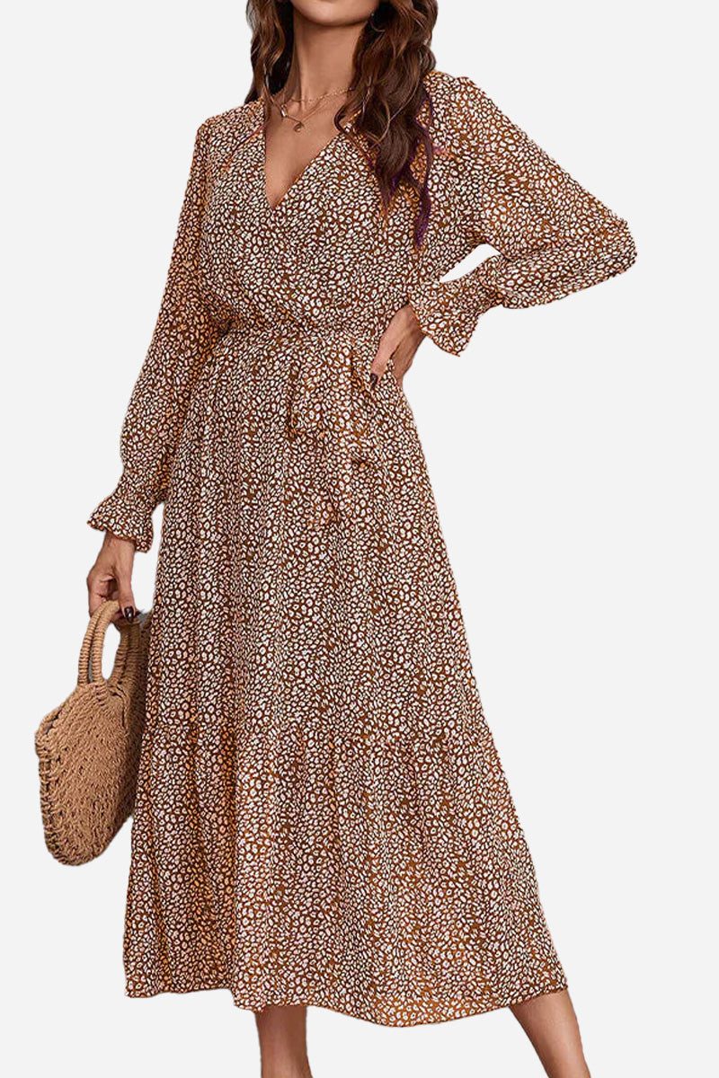 Woman wearing a floral Bloom Wrap Midi Dress with long sleeves and a waist tie holding a woven bag