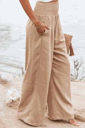 Woman wearing beige high-waist cotton linen palazzo pants with wide legs and pockets on beach