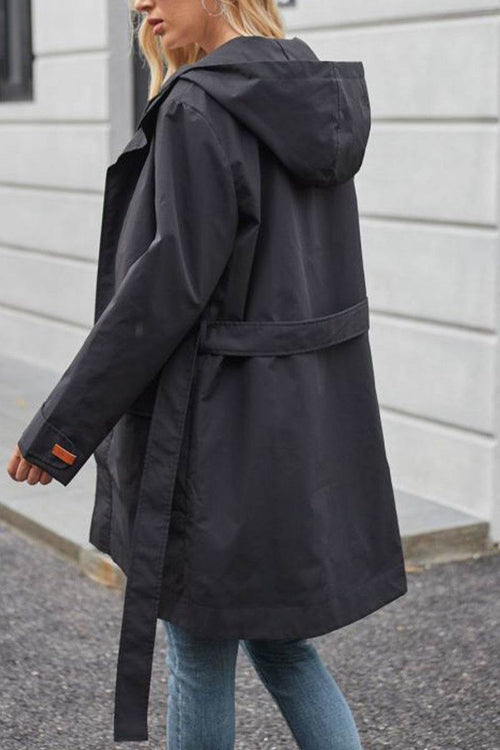 Black water-resistant windbreaker trench jacket with hood and belt worn with jeans outdoors