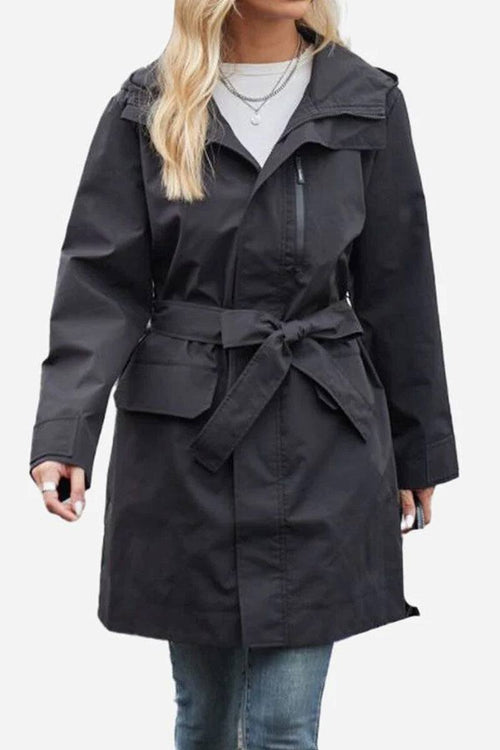 Black water-resistant windbreaker trench jacket with adjustable belt and zipper front worn with jeans
