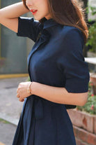 Woman wearing navy radiance belted shirt dress with collar and short sleeves outdoors