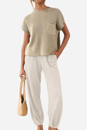 Woman wearing Comfy Couture Knit Sweater short-sleeve top with pocket and high-waisted loose pants two-piece set in neutral tones, holding a woven handbag.