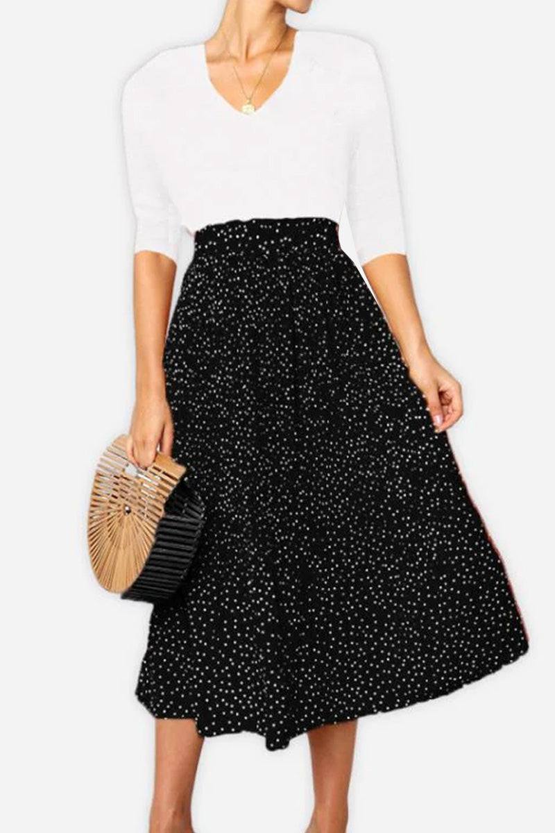 Woman wearing an effortlessly chic black polka dot pleated midi skirt with high waist and white top, holding a wooden handbag.