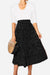 Woman wearing an effortlessly chic black polka dot pleated midi skirt with high waist and white top, holding a wooden handbag.
