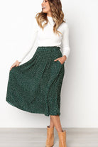 Woman wearing effortlessly chic polka dot pleated high-waist midi skirt with pockets and white long-sleeve top