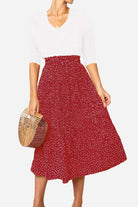Woman wearing effortlessly chic polka dot pleated high-waist midi skirt with white top and wooden handbag