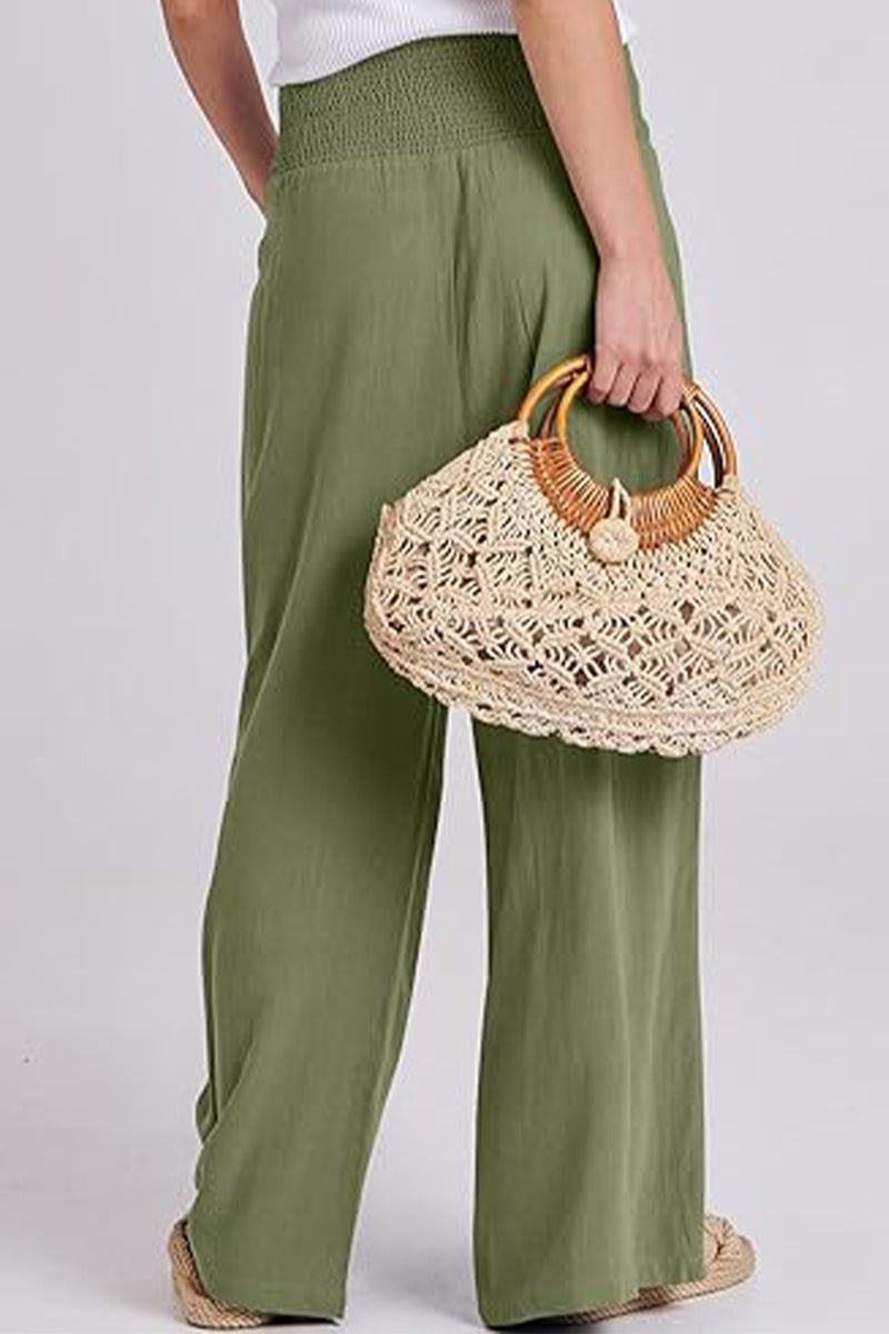 Woman wearing olive green oversized palazzo pants holding a woven straw handbag