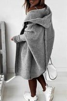Woman wearing warm oversized hooded grey cardigan with white sneakers and handbag indoors