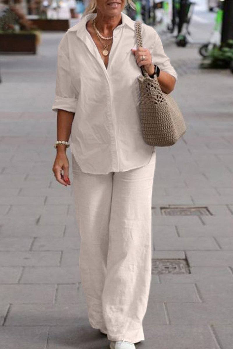 Woman wearing a relaxed white shirt and wide-legged trousers two-piece set with rolled sleeves and a beige knit handbag walking outdoors.