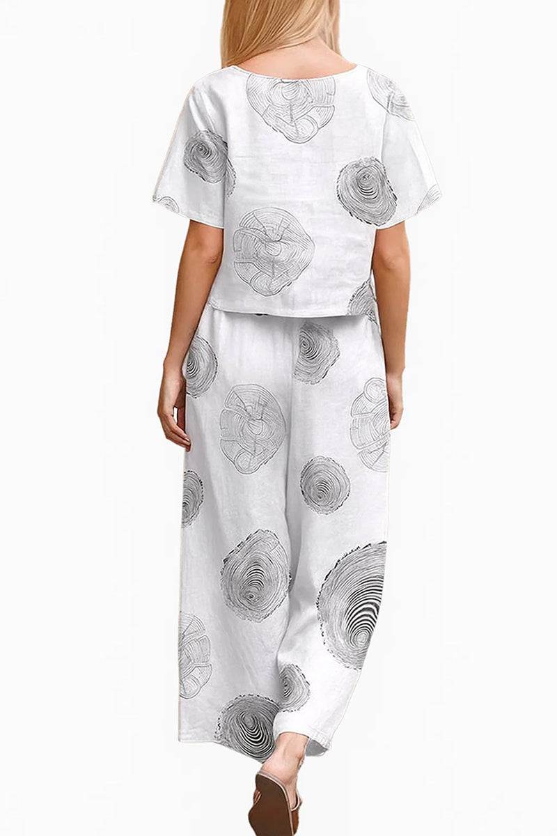 Back view of woman wearing white loose fit co-ord set with black circular floral prints, featuring a short-sleeve top and wide-leg pants.