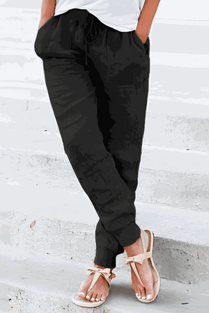 Woman wearing black relaxed chic elastic ankles pants with pockets and white top, standing on concrete steps