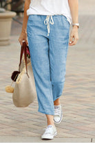 Woman wearing light blue relaxed fit straight pants with drawstring waist and white sneakers walking outdoors carrying a beige tote bag