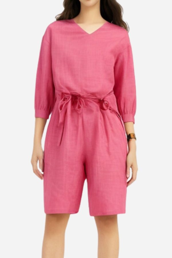 Woman wearing a pink cotton two-piece set with a loose V-neck shirt and high-waisted knee-length shorts with pockets.