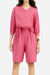 Woman wearing a pink cotton two-piece set with a loose V-neck shirt and high-waisted knee-length shorts with pockets.