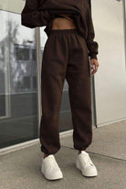 Woman wearing brown cotton-blended two-piece tracksuit pants with white sneakers outdoors.