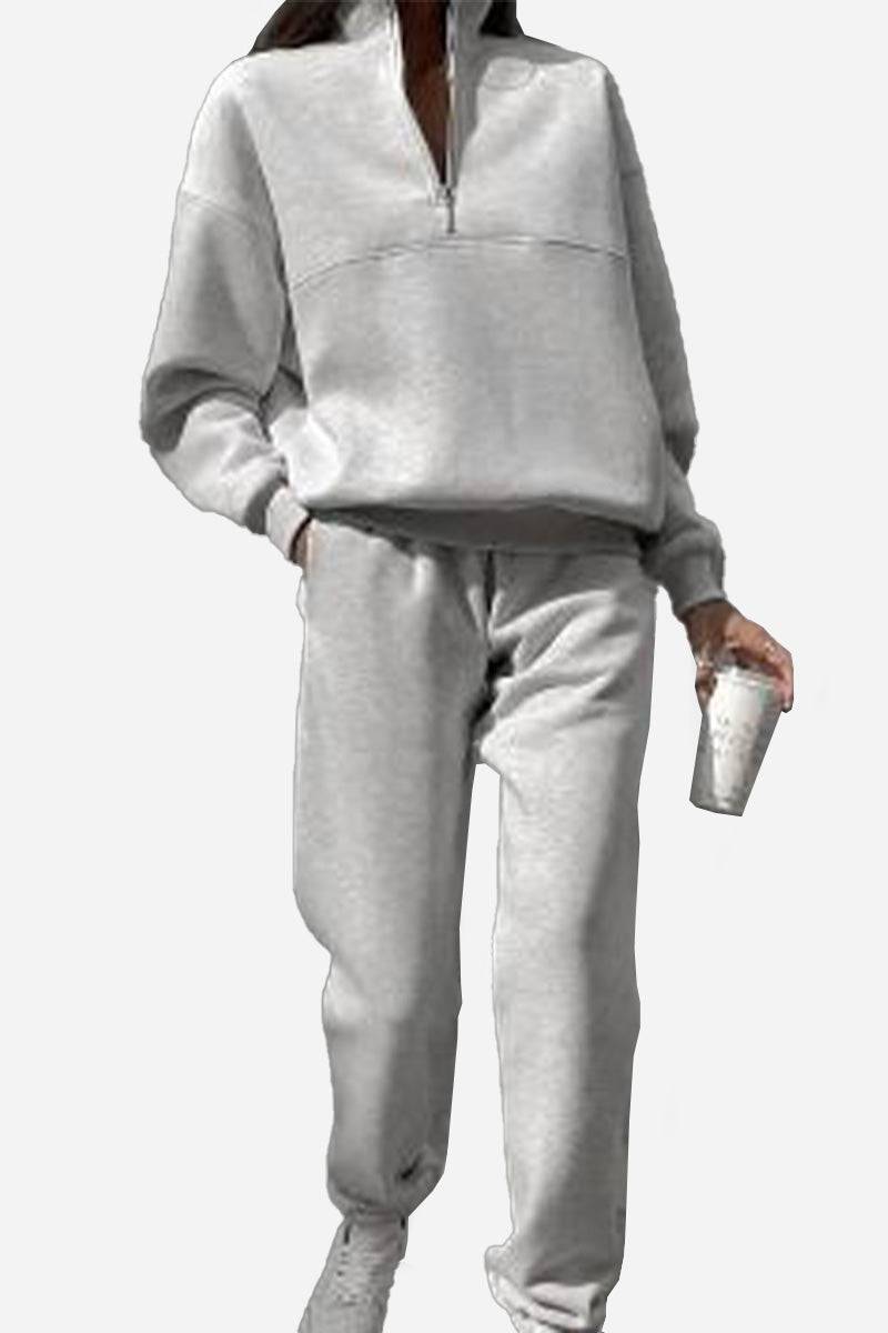 Woman wearing grey cotton-blended two-piece tracksuit with high collar and zipper, holding a cup