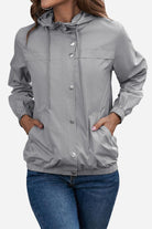 Woman wearing light grey outdoor hooded raincoat and windbreaker with button closure and elastic cuffs