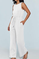 Woman wearing white sleeveless wide leg pants jumpsuit with drawstring waist and pockets