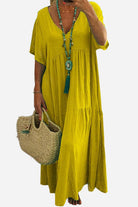 Yellow V-neck two-tiered maxi swing dress with loose sleeves and flowy silhouette worn with turquoise necklace and woven bag
