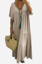 Beige V-neck two-tiered maxi swing dress with loose sleeves and flowing tiers, styled with a turquoise necklace and woven handbag