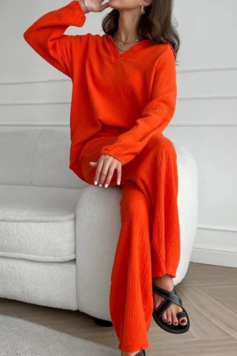 Woman wearing bright orange cotton collared two-piece set with bishop sleeves sitting on white couch