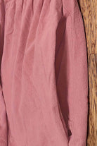 Close-up of pink capped-sleeve voluminous pleated midi dress fabric with pocket detail on wooden floor