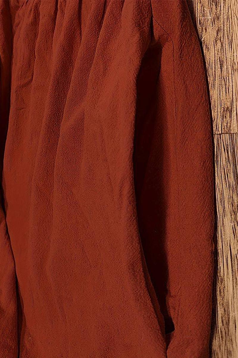 Close-up of rust-colored capped-sleeve voluminous pleated midi dress fabric and pocket detail on wooden floor