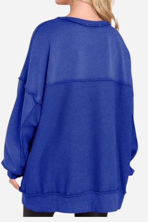 Back view of a woman wearing a blue oversized urban sweatshirt with slouchy sleeves and raw seam detailing.