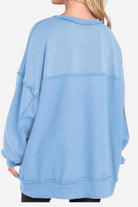 Back view of a light blue oversized urban sweatshirt with a slouchy fit and raw seam details worn by a person with blonde hair.