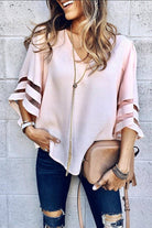 Woman wearing pink mesh panel sleeve loose fit top with distressed jeans and beige purse