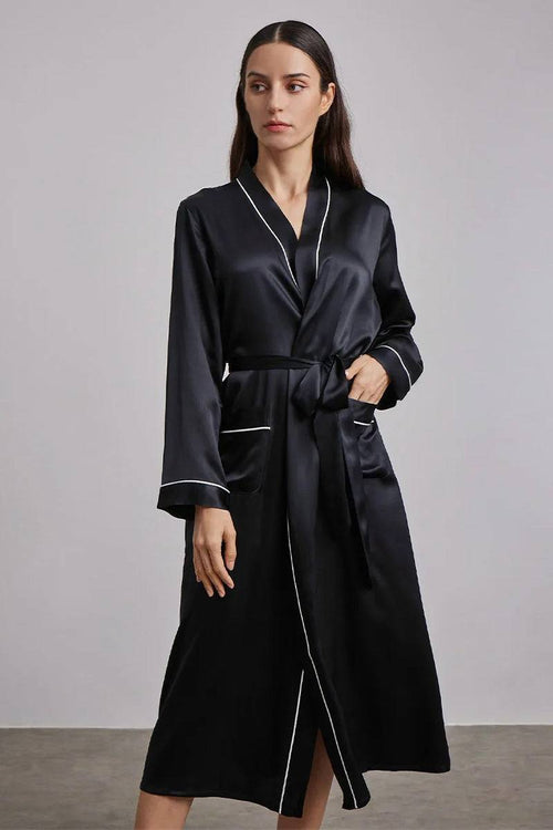 Woman wearing black Mulberry Silk Nightgown with long sleeves and sash belt standing against gray background