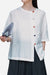 White regenerated cellulose blouse with asymmetrical colorful buttons, oversized fit, and short sleeves, styled with dark pants and holding a fan.
