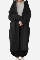 Oversized black buttoned hooded coat on person wearing casual outfit