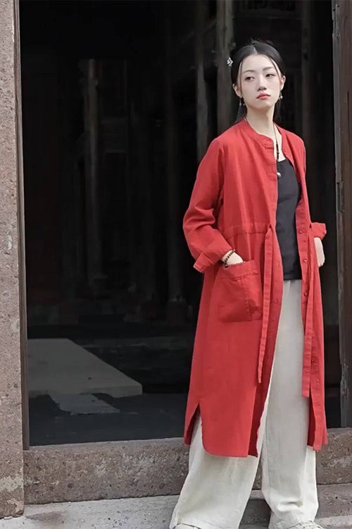 Woman wearing oversized casual loose red ramie linen cardigan with pockets and beige wide-leg pants standing by doorway