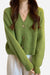 Green casual loose boxy cardigan with large buttons, ribbed texture, and relaxed fit worn over white pants.