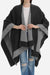 Elegant knitted poncho in two-tone black and gray draped over casual outfit with jeans and white top.