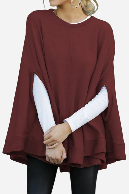 Woman wearing elegant burgundy poncho pullover with long white sleeves and black pants.