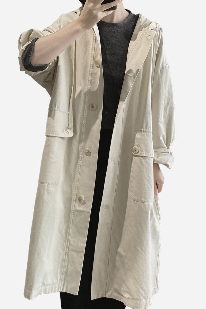 One size travel-ready hooded windbreaker in natural cotton with snap buttons and pockets, worn over casual black outfit.