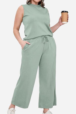 Woman wearing cotton chic sleeveless two-piece set in sage green with pockets and wide-leg pants holding a coffee cup