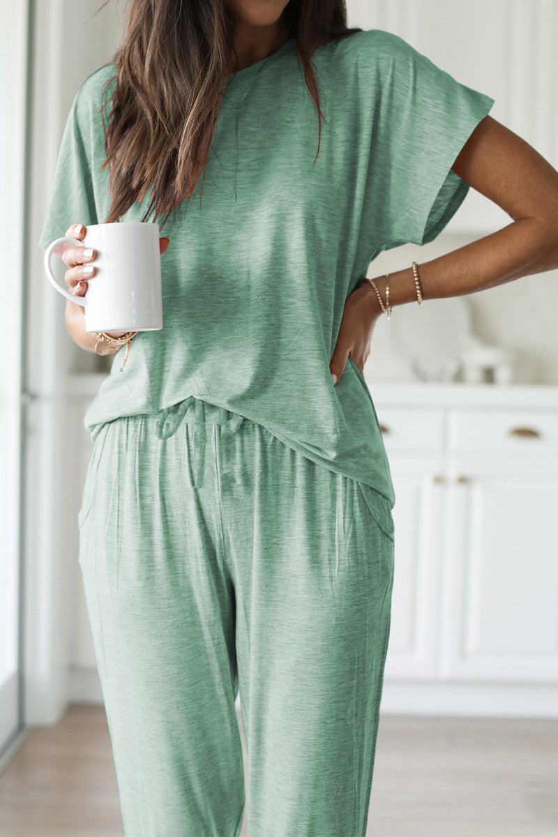Woman wearing green ultra-soft two-piece loungewear set with batwing sleeves and jogger pants holding a white mug indoors