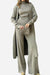 Woman wearing a one-size-fits-all premium three-piece collection in soft, breathable fabric with a long cardigan, ribbed turtleneck top, and wide-leg pants in neutral beige tone