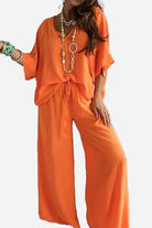 Woman wearing an elegant orange two-piece pantsuit with a V-neck top and wide-leg pants, accessorized with layered necklaces and bracelets.