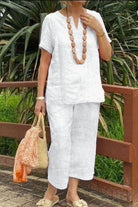 Woman wearing white Breezy Cotton Blend relaxed fit two-piece set with short sleeves and elastic waist pants, accessorized with wooden bead necklace and straw bag.