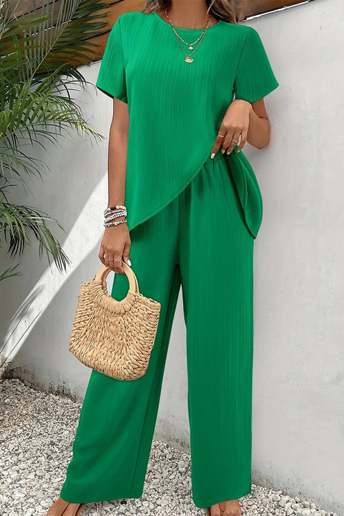 Green textured elegance two-piece set with asymmetrical top and wide-leg pants, styled with a woven handbag and jewelry.